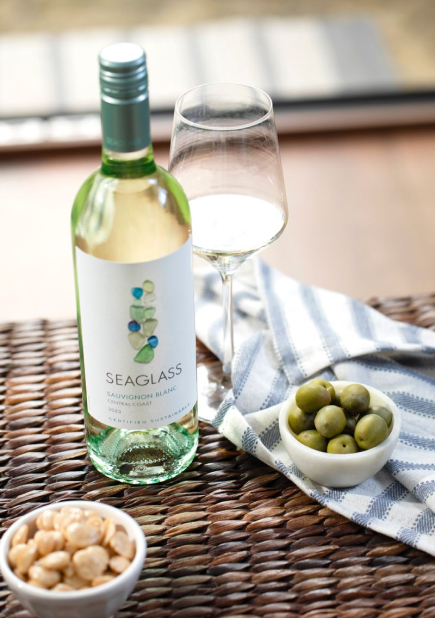 A bottle of Seaglass sauvignon blanc white wine next to small bowls of green olives and nuts